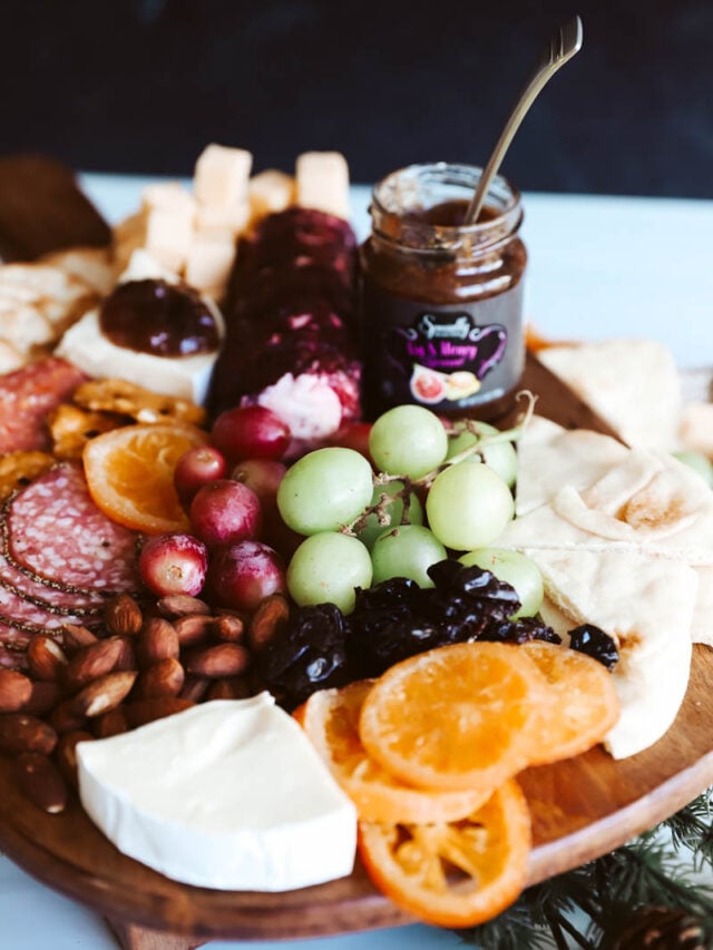 a cutting board layered with charcuterie food and jams
