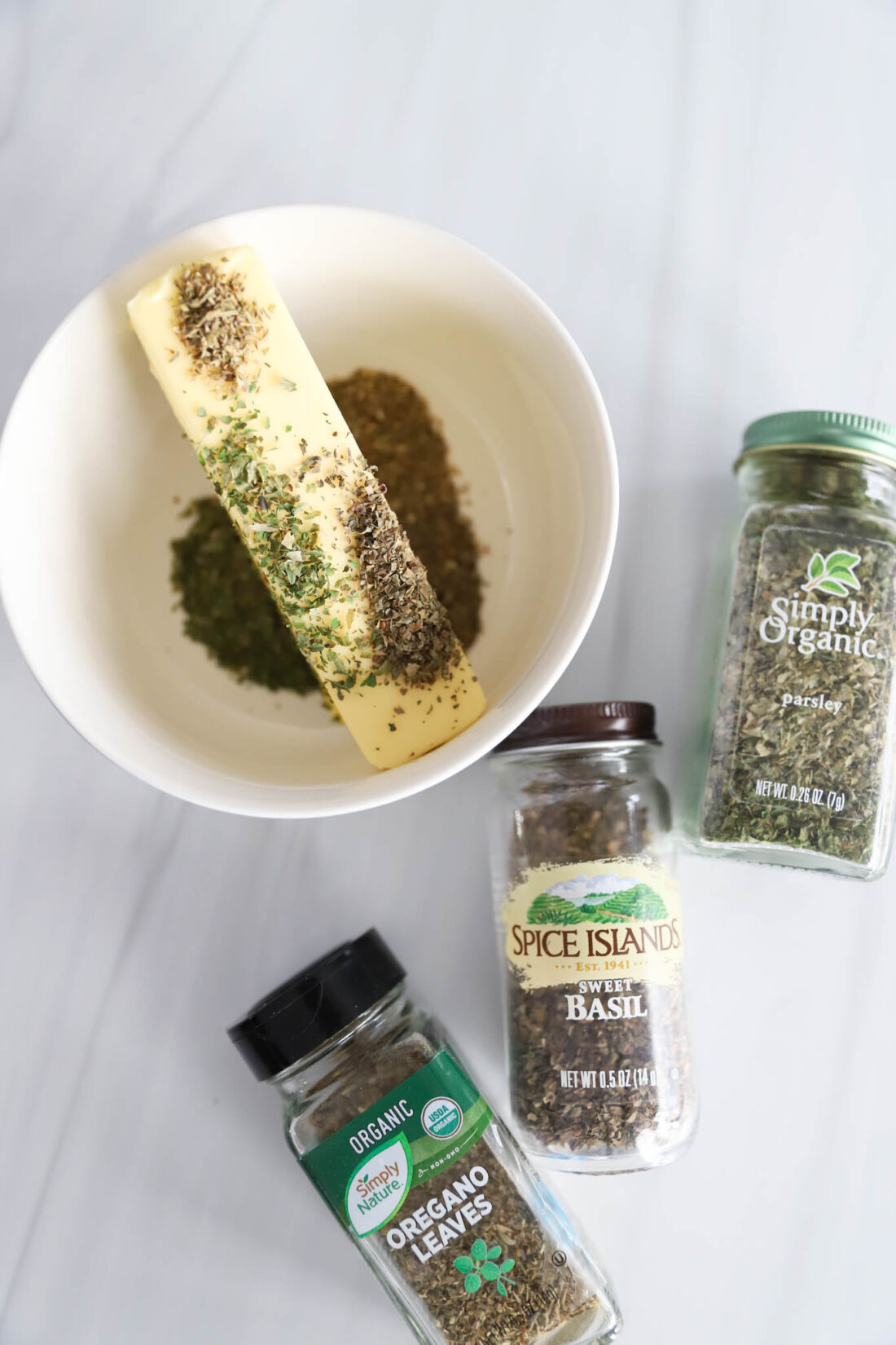 ingredients for herbed butter in a white bowl.