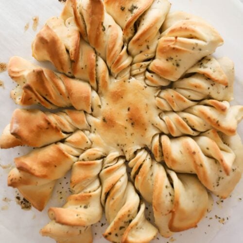Easy Garlic Bread Wreath If you're a fan of garlic bread, you're going to love this festive twist on a classic favorite. The garlic bread wreath is a great recipe that's perfect for holiday gatherings or any occasion where you want to impress your guests with something delicious and unique. The best part? It's made with simple ingredients that you probably already have in your pantry. To make this garlic bread wreath, you'll need a few basic ingredients like pizza dough, garlic, butter, Italian seasoning, and Parmesan cheese. The recipe is easy to follow and can be adapted to your personal taste preferences. Whether you like your garlic bread extra garlicky or prefer a milder flavor, you can adjust the recipe to suit your needs. You can use store bought pizza crust that is ready to go, or make your own pizza dough. I have a delicious, tried and true pizza crust recipe if you want to try that! While I made this into a wreath, you can also do simple garlic bread twists and eat them like you would homemade breadsticks. Anything that contains herb butter and fresh bread is a winner, in my book. Why you'll love this recipe Ease- This recipe is easy and allows you to use premade crust or make your own. You can toss the ingredients in the bowl of a stand mixer to make it extra simple. Or, you can mix things up in a large bowl and knead it until elastic. Flavor- This is a great side to have with any Italian style dish and one of my favorite things is that the garlic twists are easy to pull away from the wreath and dip in a garlic butter sauce or marinara sauce. Kid-friendly- This is a delicious dish that every kid loves. It helps fill hungry bellies without too much effort. Ingredients To make this delicious garlic bread wreath, you will need the following ingredients: Pizza Dough- You may use store-bought dough or homemade dough. You will need two packages so that you will have enough for a top and bottom crust. Butter- If you forget to set your butter out ahead of time, you may use melted butter. I do find that soft butter works better when spreading because it isn't as messy. Garlic powder or garlic salt Parmesan cheese Italian seasoning- If you don't have Italian seasoning on hand, use a combination of dried basil, oregano, and parsley. How to make a Garlic Bread Wreath While this seems like a fancy recipe, it really is quite simple. You make your pizza crust, roll it out, cover it in herbed butter, slice, and twist. Roll out the Pizza Dough- On a lightly floured surface, roll out your pizza dough and take a dinner plate and lay it on top of the dough. With a sharp knife or pizza cutter, cut around the outside of the plate to form a large circle of dough. Lay the dough on parchment paper. Add the Garlic Butter- Just like you would with homemade garlic knots, spread the herb butter on top of the crust with a rubber spatula or the back of a wooden spoon. Sprinkle with parmesan cheese. Cut the wreath twists- Roll out and cut the top piece of dough just as you did the bottom piece. Lay the top piece on top of the garlicky breadstick dough. Put a glass in the middle of the circle and slice 3/4 inch to 1 inch slices in the dough, stopping at the glass. Twist them in the same direction. Bake on a greased baking sheet or parchment lined baking sheet. This recipe is a great idea for pizza night, pasta night, or even a dinner party. It's a little twist on traditional garlic bread that's sure to impress your family. The best part is that it's one of the easiest breads to make, even if it's your first time handling pizza or bread dough. If you're making this ahead of time, you can place your wreath in the refrigerator for 2 hours prior to baking it. What to serve with Garlic Parmesan Twists Garlic bread wreath is a delightful and versatile side dish that can be served as a side or a main dish. It pairs well with a variety of dishes, including your favorite soup, a pasta dish, or a main dish. You can also serve it as an appetizer or a snack. To make your garlic bread wreath even more delicious, you can serve it with some accompaniments. Try serving it with a tomato sauce for dipping or some melted cheese on top. You can also add some herbs or spices to the butter mixture to give it an extra kick of flavor. Storage Tips If you have leftovers, you can store your garlic bread wreath in an airtight container for 2-3 days. Make sure to let it cool completely before storing it. To reheat, simply wrap it in foil and heat it in the oven for a few minutes. If you want to enjoy your garlic bread wreath later in the week, you can freeze it. Wrap it tightly in foil and place it in a freezer-safe container. It will keep for up to a week in the freezer. To reheat, simply thaw it in the fridge overnight and then reheat it in the oven. It's important to note that garlic bread wreath is best enjoyed fresh. While it can be stored and reheated, it may not be as delicious as when it's freshly baked. So, if you want to enjoy the full flavor and texture of your garlic bread wreath, it's best to eat it on the same day you bake it.