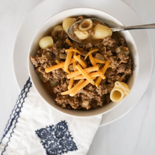 Homemade Hamburger helper in a white bowl with shredded cheese on top.