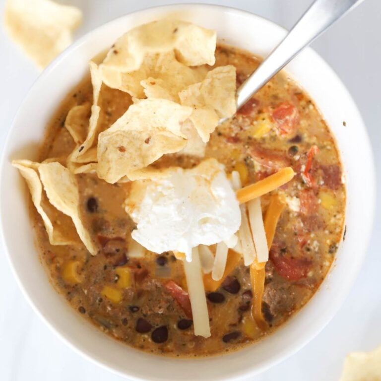 Creamy taco soup in a white bowl with shredded cheese and taco chips.