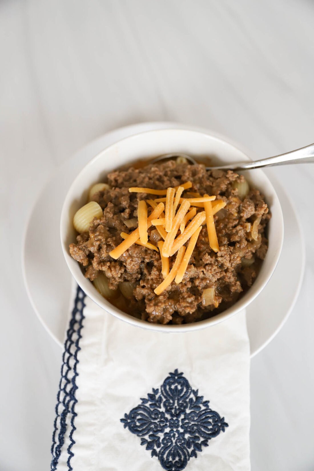 Noodle shells with a meat mixture and shredded cheddar cheese on top in a white bowl.