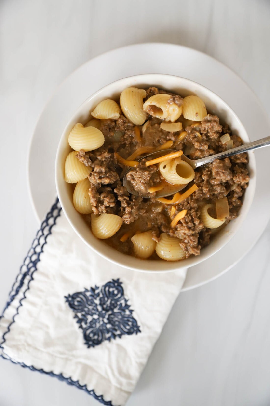 Crock pot hamburger helper and shredded cheddar cheese on top in a white bowl.