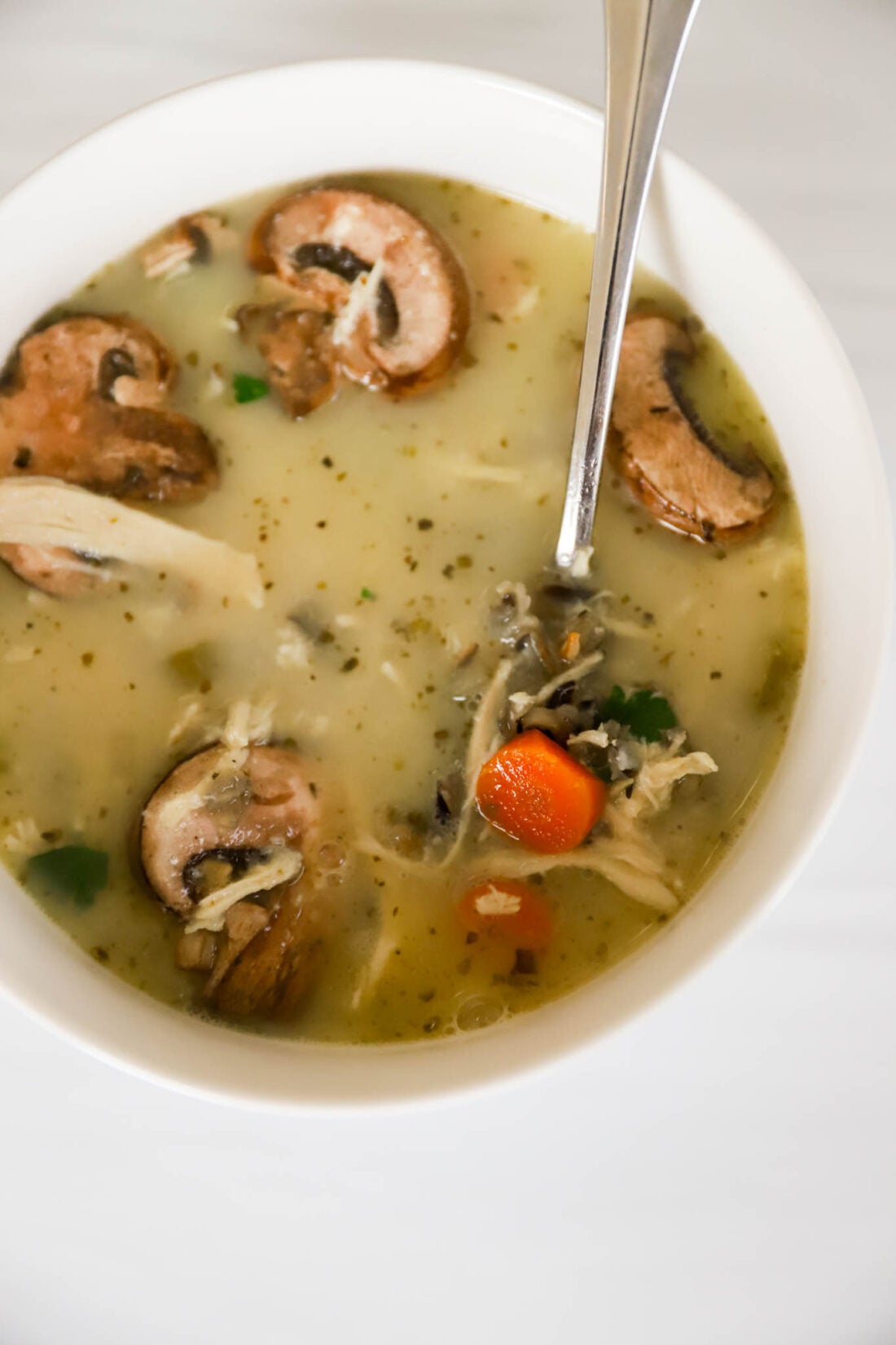 White bowl with wild rice and chicken soup with mushrooms in it.