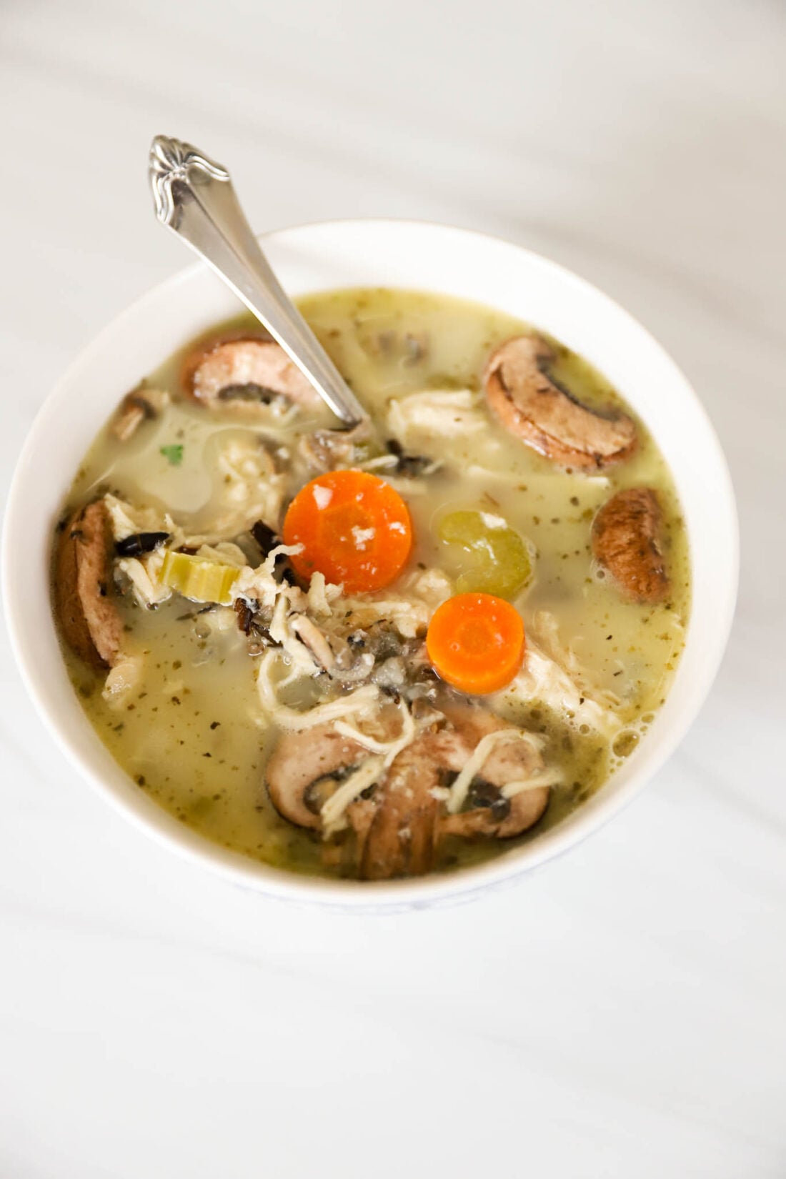 White bowl with wild rice and chicken soup with mushrooms in it.