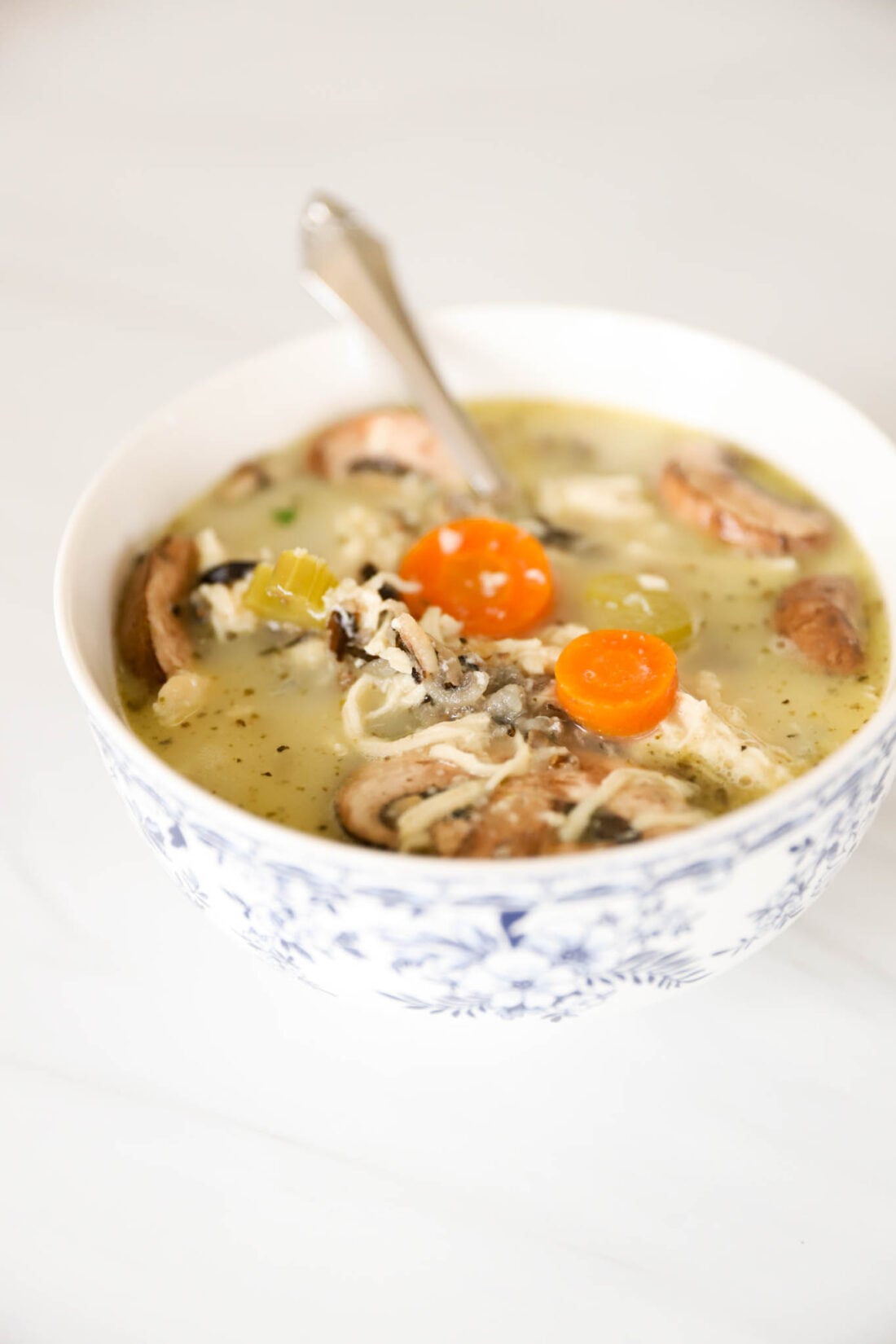 White bowl with wild rice and chicken soup with mushrooms in it.