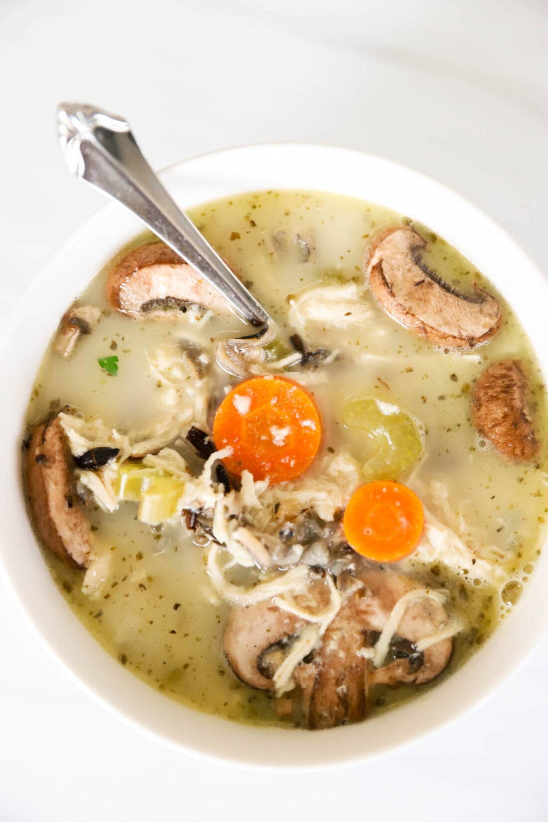 White bowl with wild rice and chicken soup with mushrooms in it.