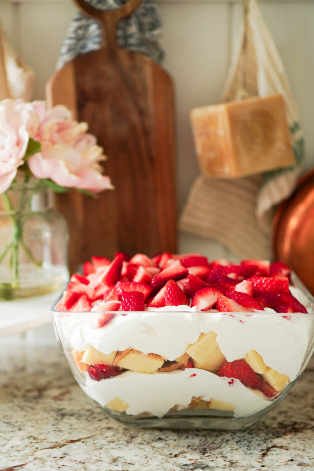 Clear glass trifle bowl filled with pound cake, whipped cream, and chopped strawberries.