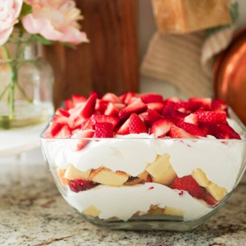 Clear glass trifle bowl filled with pound cake, whipped cream, and chopped strawberries.