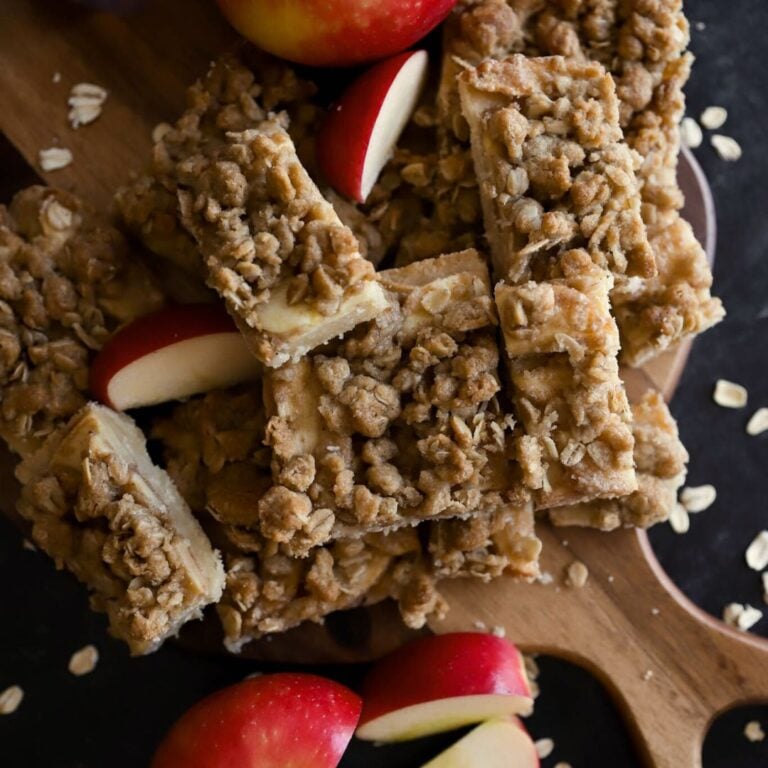 dessert bars with oatmeal topping on a cutting board with red apples next to them